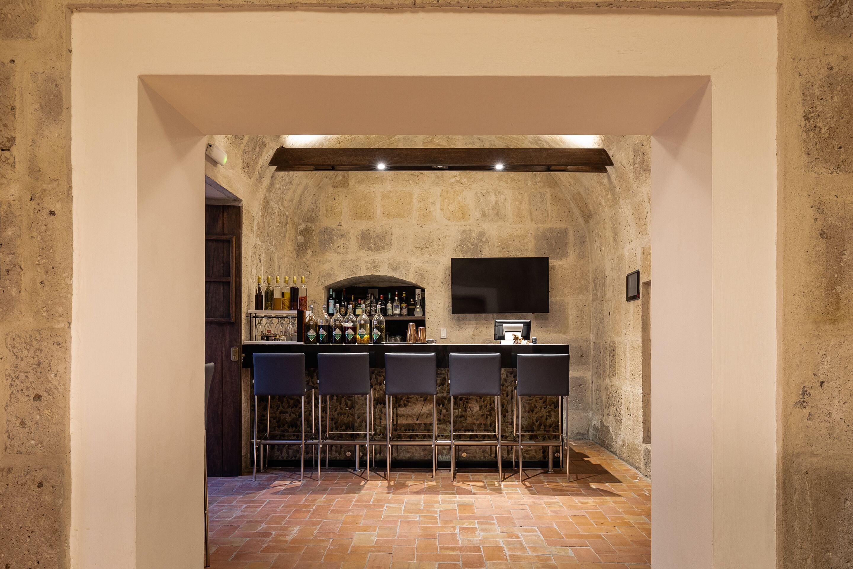 A bar area with a stone wall, a flat-screen TV, and a bar counter with stools.