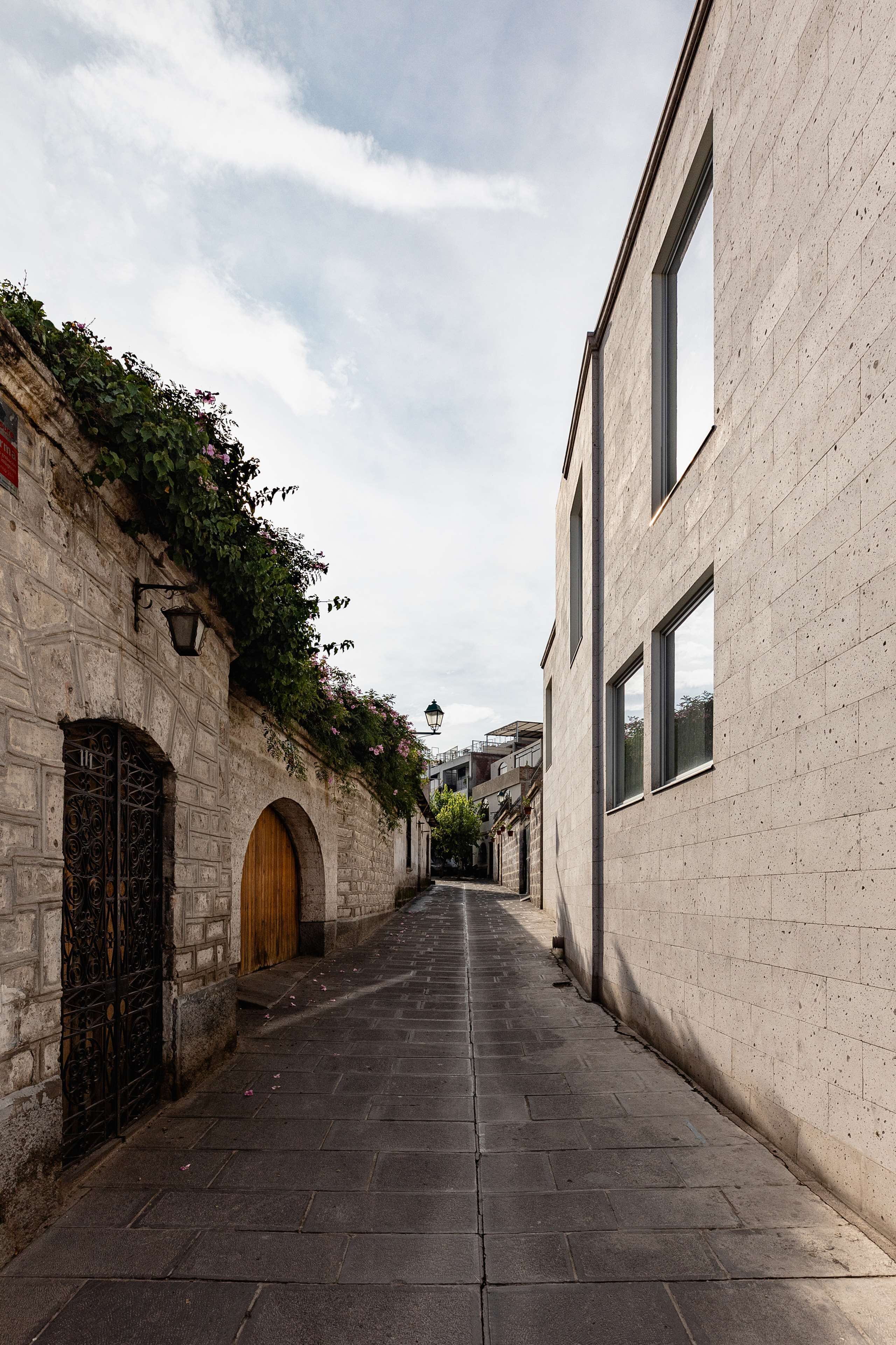 Un callejón estrecho con un edificio de piedra en un lado y uno moderno en el otro.