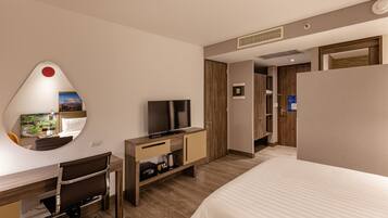 Una habitación de hotel con cama, escritorio con silla, televisor, espejo y armario.