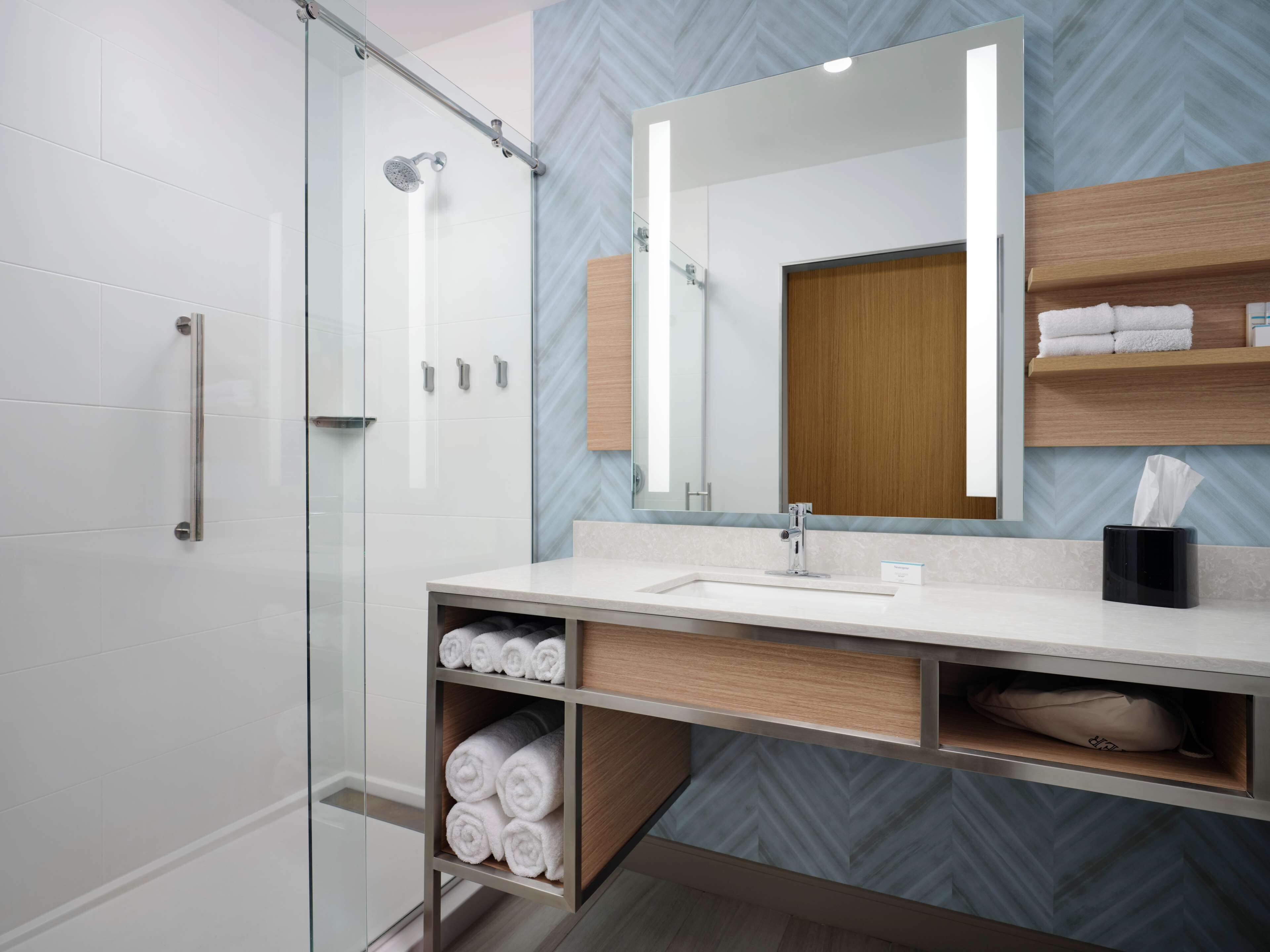 Een moderne badkamer met een douchecabine van glas, een grote spiegel en houten opbergplanken.