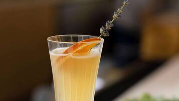 A tall glass with a layered drink, garnished with an orange peel and a sprig of lavender.