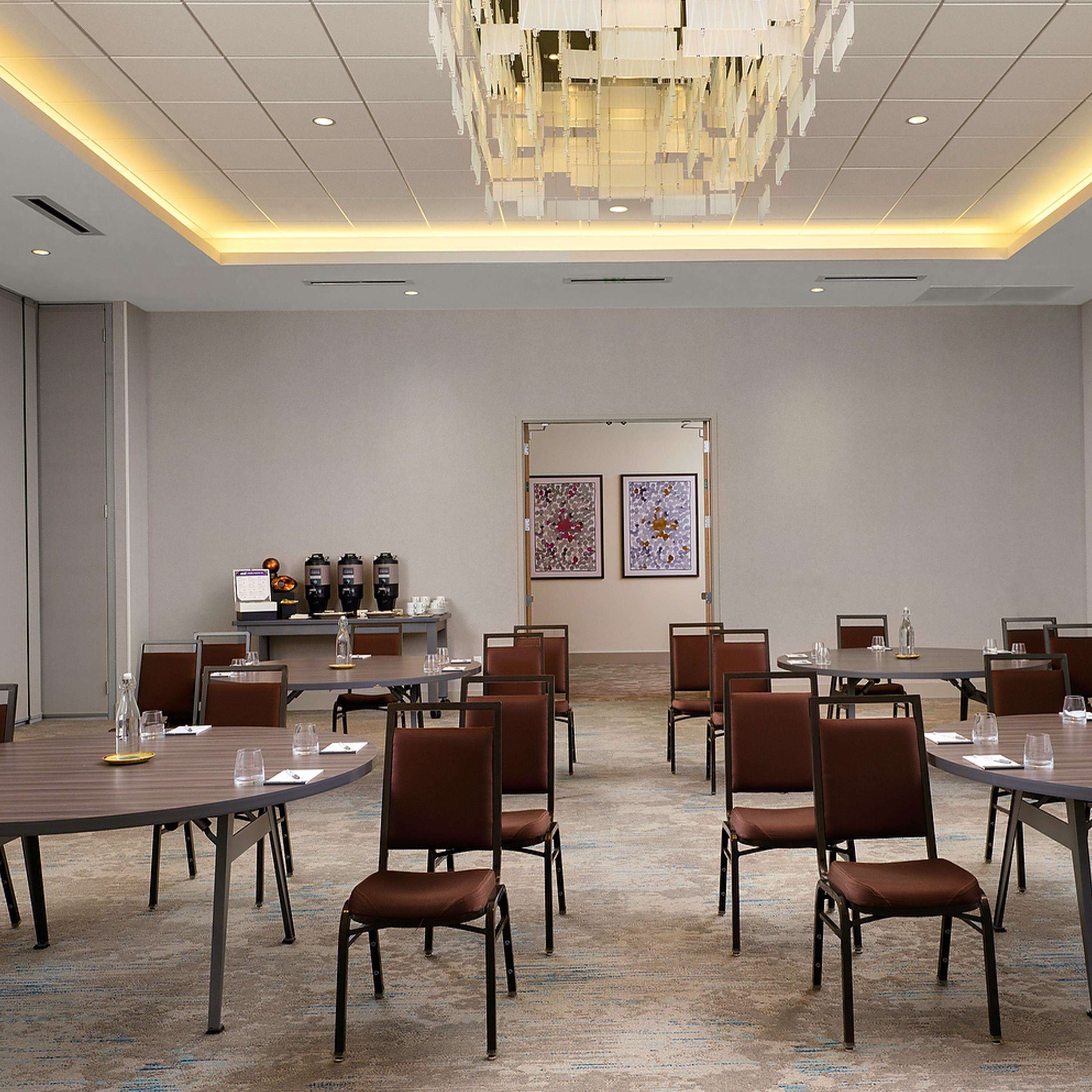 A conference room with multiple tables and chairs, a coffee station, and artwork on the wall.