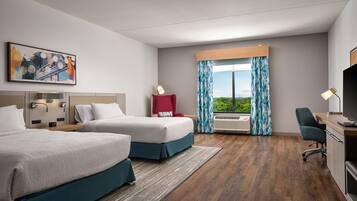 Habitación de hotel con dos camas, un escritorio, una silla, un televisor, una ventana con cortinas, un cuadro y un equipo de aire acondicionado.