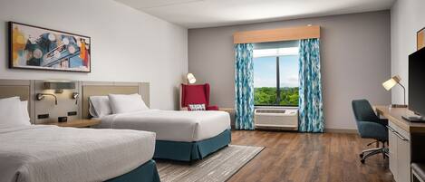 A hotel room with two beds, a desk, a chair, a TV, a window with curtains, a painting, and an air conditioning unit.