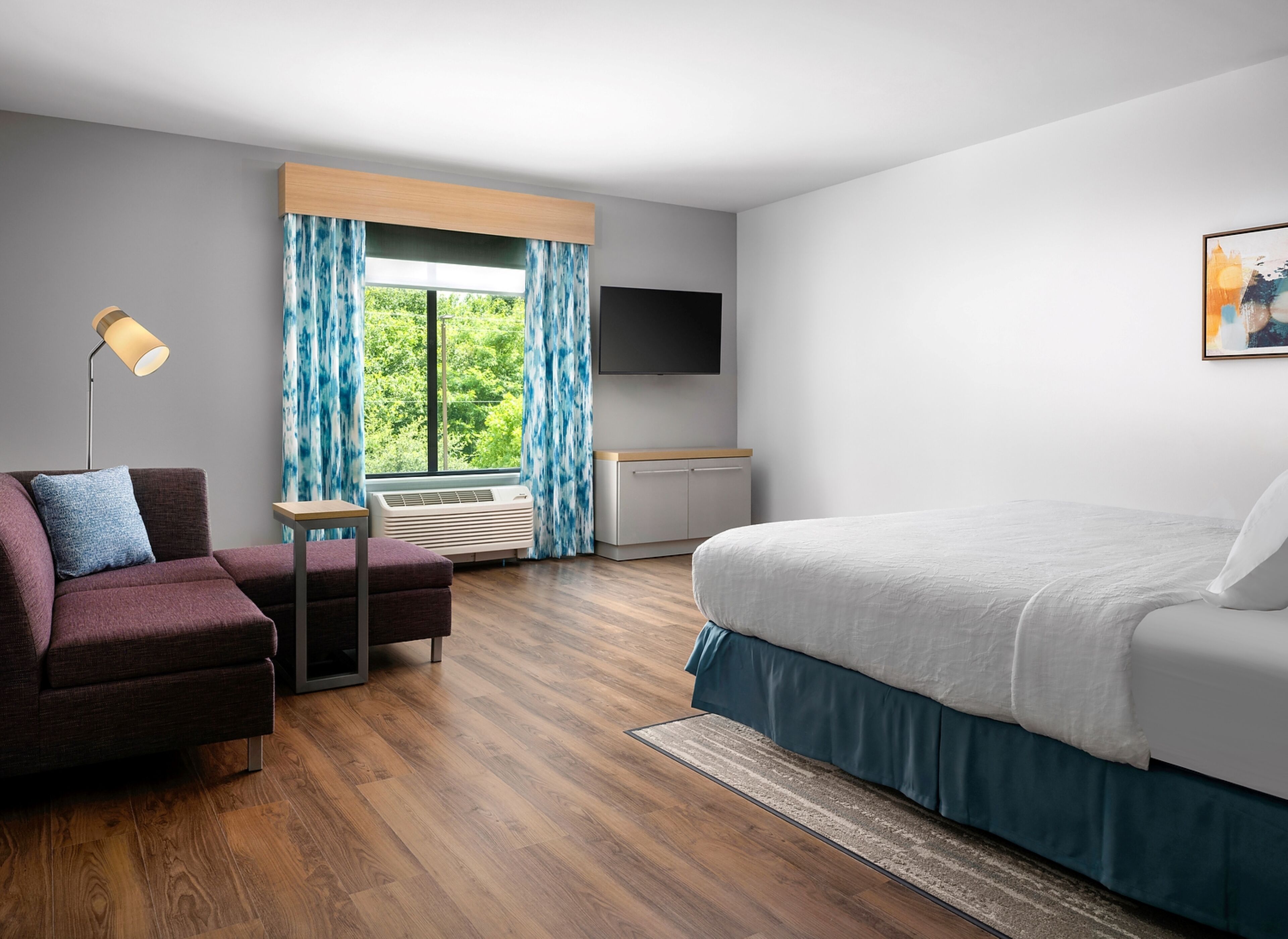 A modern hotel room with a bed, a desk, a chair, a TV, and a window with curtains.