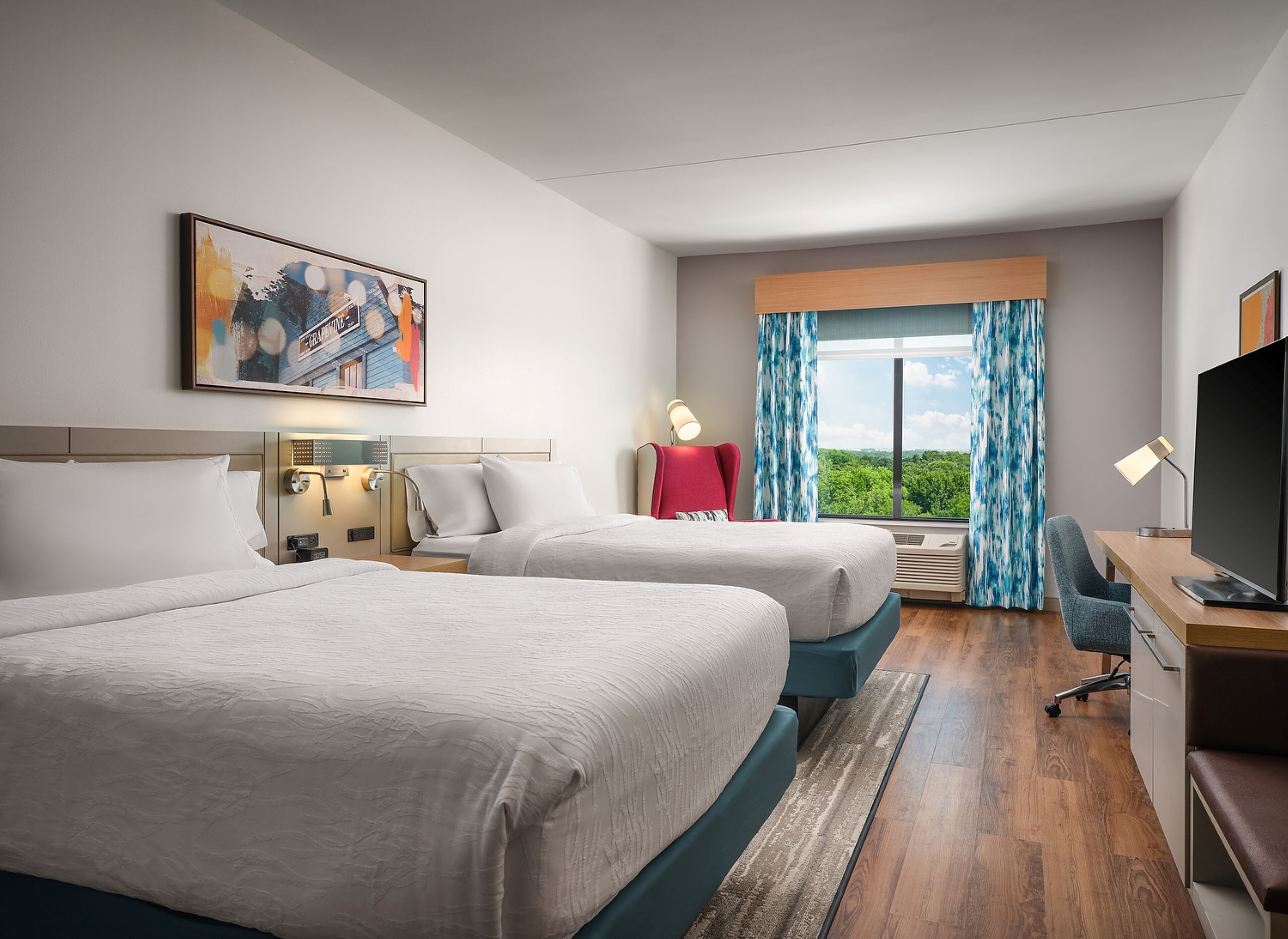 A hotel room with two beds, a desk with a TV, a chair, a window with curtains, and a painting on the wall.