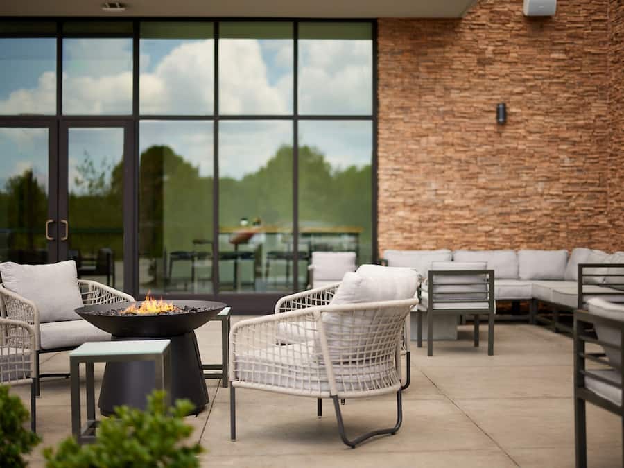 Un patio al aire libre con mobiliario de mimbre, una chimenea y vistas al exterior a través de amplias ventanas.