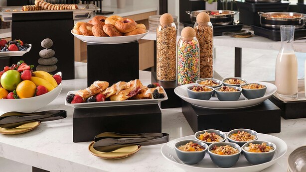 A buffet setup with various food items, including pastries, fruits, cereals, and beverages. - Hilton Garden Inn Grapevine at Silverlake Crossing (Grapevine)