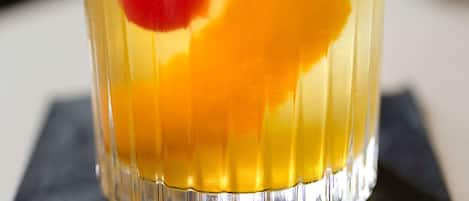 A clear glass with a layered drink, ice cubes, and a red garnish on a dark surface.