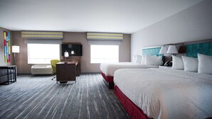 A hotel room with a large bed, a desk, a chair, a TV, and a window.