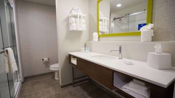 A modern bathroom with a white sink, a mirror with a yellow frame, and a glass shower enclosure.