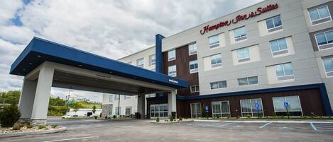 A Hampton Inn & Suites hotel with a clear sky, parking lot, and a blue canopy over the entrance.