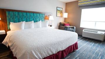 A hotel room with a large bed, a headboard with a geometric pattern, a chair, a lamp, and a window with a view of a landscape.