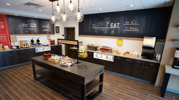 A breakfast area with a central table displaying various food items, a chalkboard menu, and a coffee station.