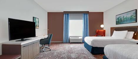 Ein Hotelzimmer mit Flachbildfernseher, Schreibtisch, Stuhl, zwei Betten, einem großen Fenster mit Vorhängen, einem Bild an der Wand und einer Lampe.