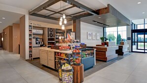 A modern hotel lobby with a reception desk, a coffee shop area, and a view of the outdoors. - Hilton Garden Inn Madison Huntsville Airport (Madison)