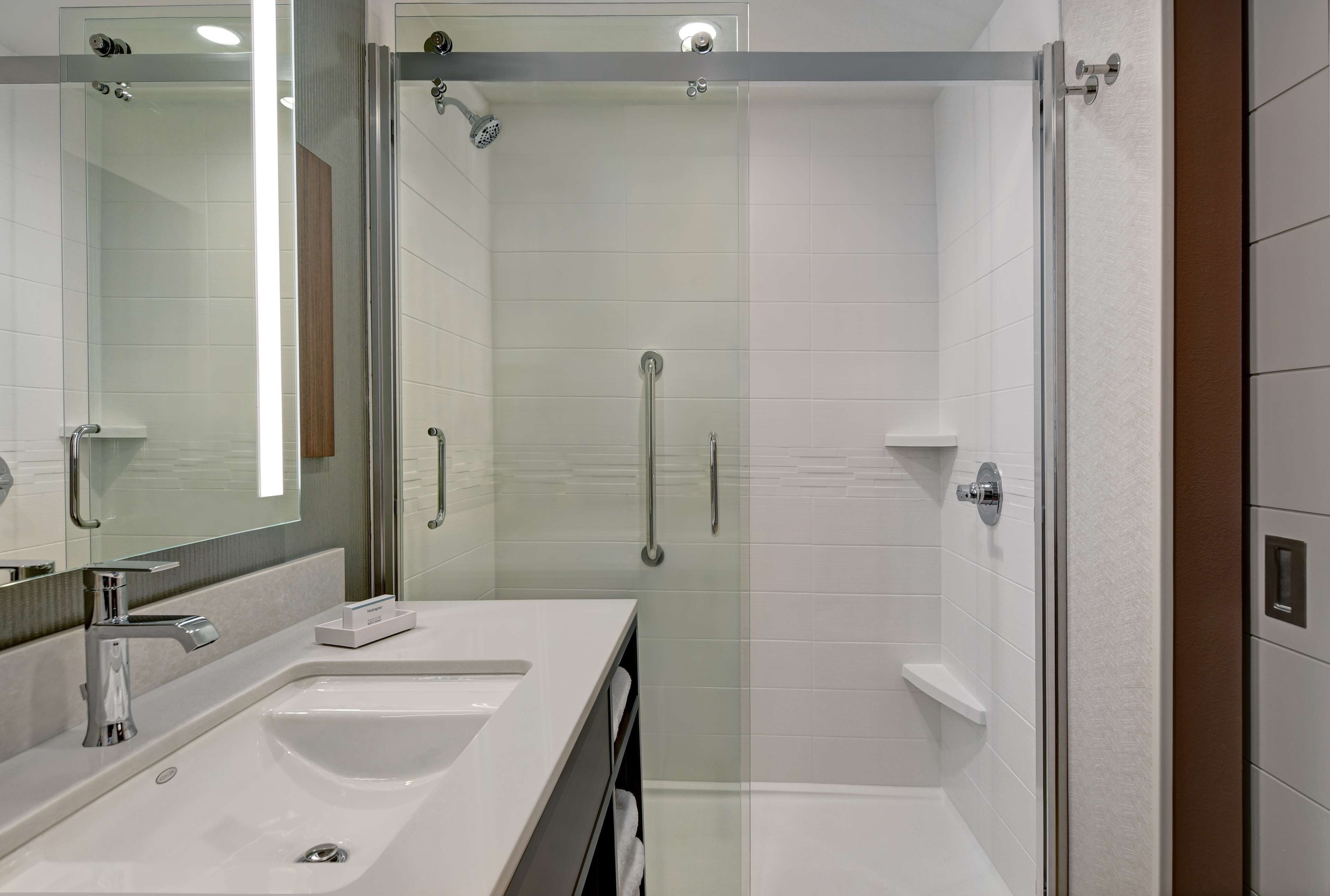 A modern bathroom with a glass-enclosed shower, a large mirror, and a white sink.