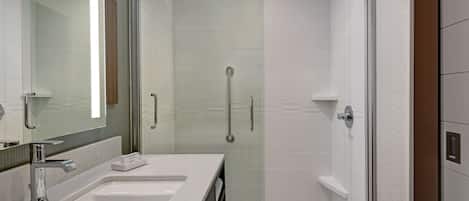 Un baño moderno con ducha de vidrio, un espejo grande y un lavamanos blanco.