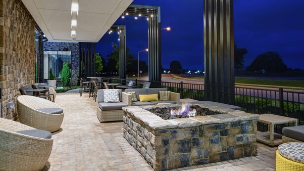 An outdoor patio with stone flooring, wicker furniture, and a stone fire pit. - Hilton Garden Inn Madison Huntsville Airport (Madison)
