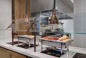 A buffet area with clear glass partitions and stainless steel serving dishes.