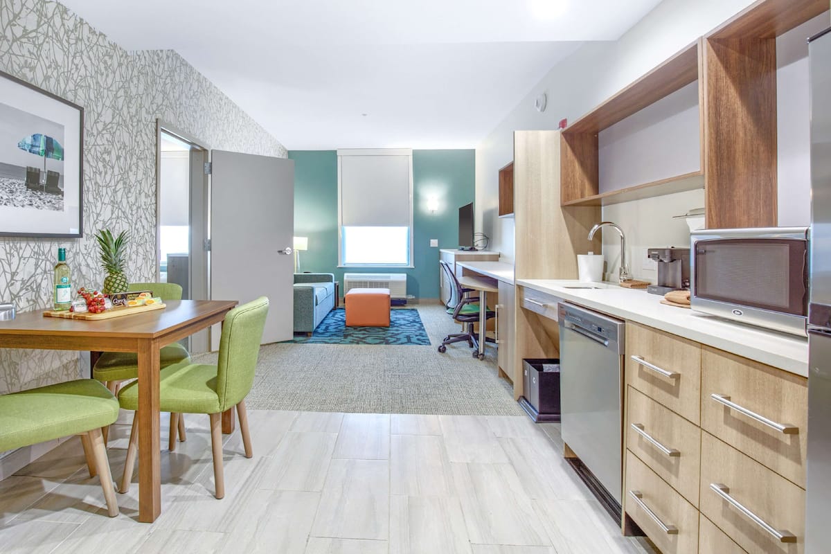 A modern kitchen with wooden cabinets, a microwave, and a dining area with a table and chairs.