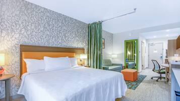 A hotel room with a large bed, a desk, a chair, and a small seating area.