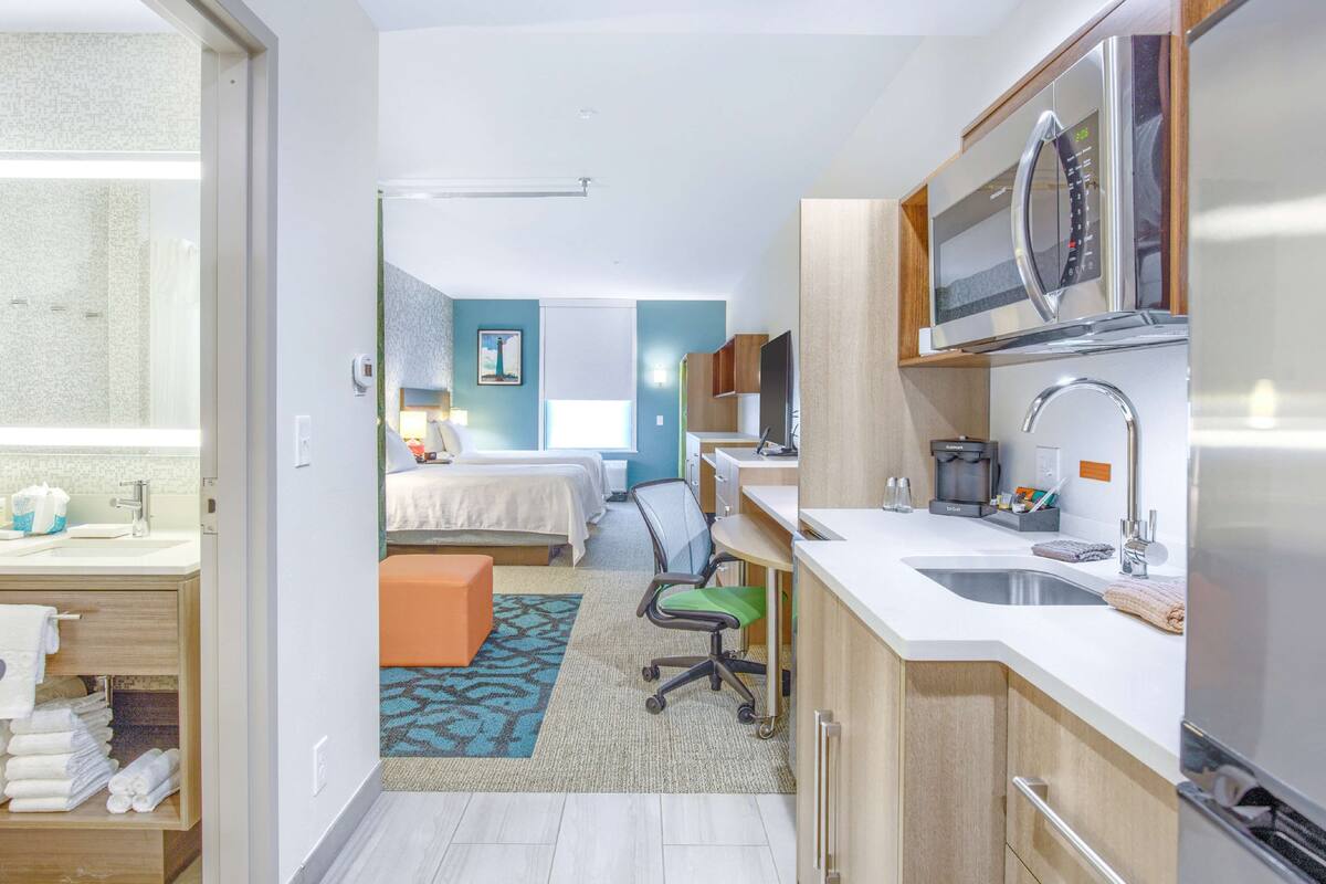 A hotel room with a kitchenette, a bed, a desk, and a bathroom.