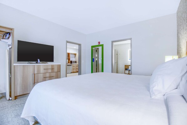 A hotel room with a large bed, a flat-screen TV, a wooden dresser, and a green-framed door.