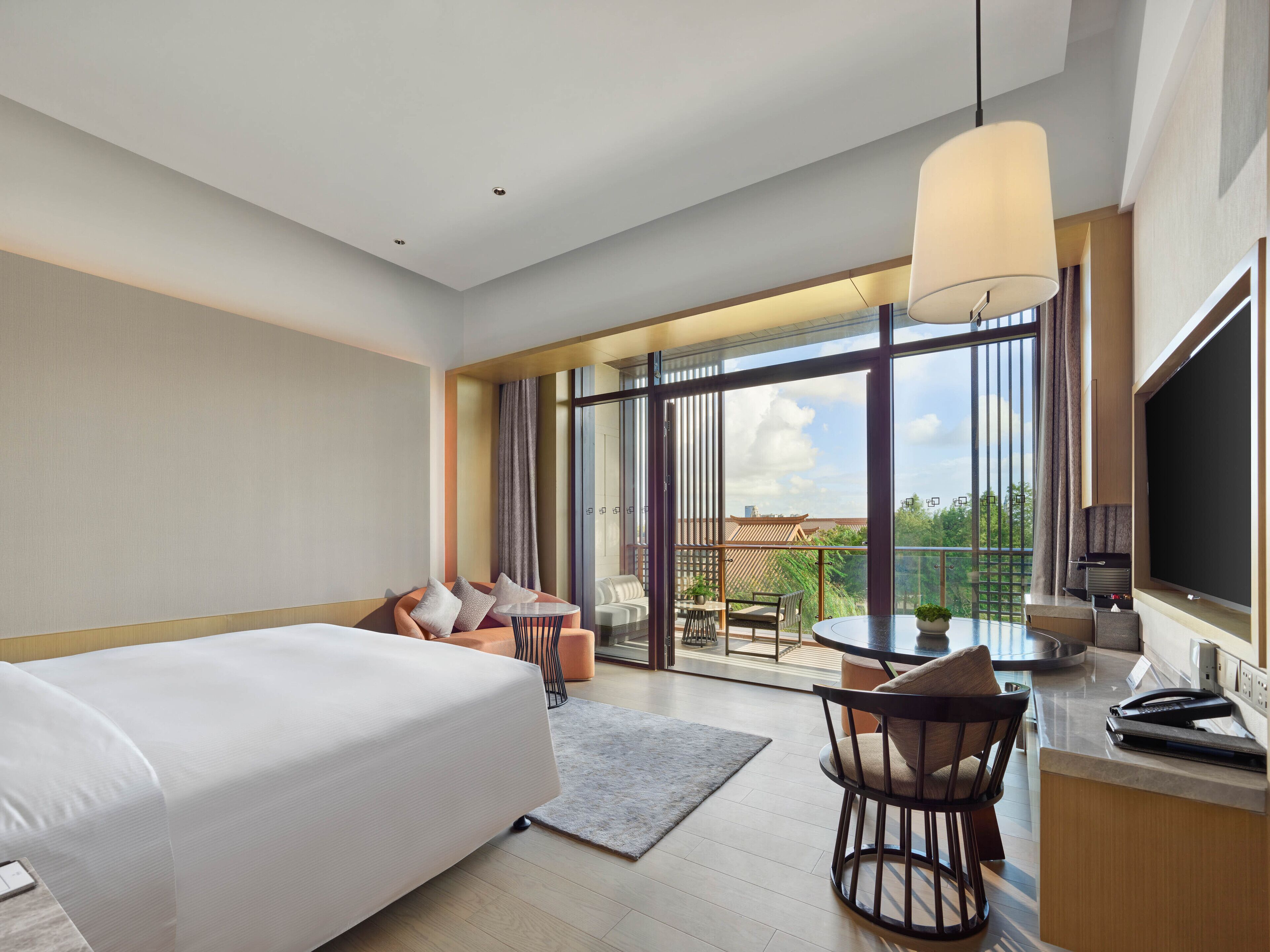 Une chambre d’hôtel moderne dotée d’un grand lit, d’un bureau avec une chaise, d’un coin repas avec une table et des chaises, et d’un balcon offrant une vue sur la ville.
