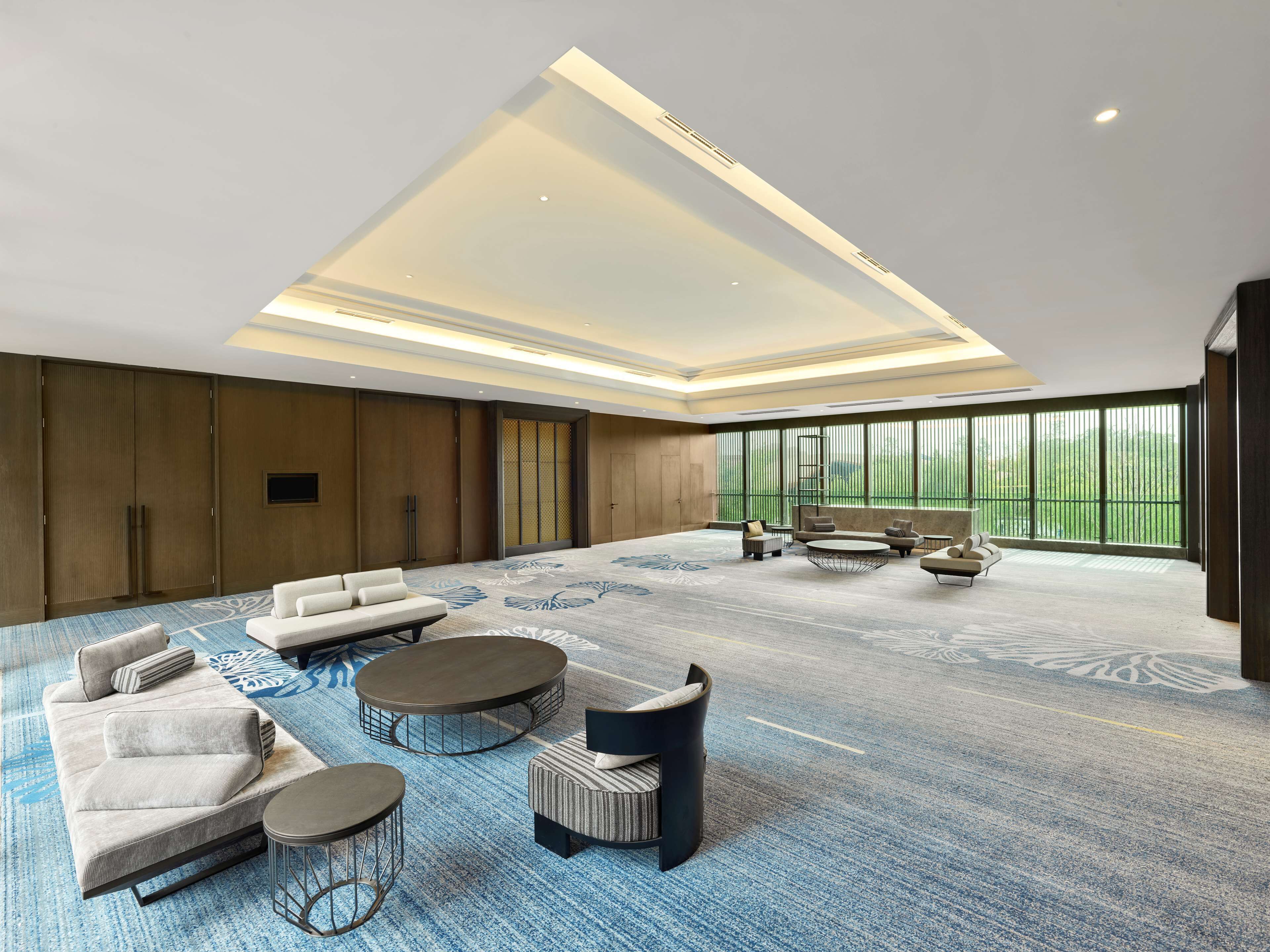 A spacious room with a high ceiling, large windows, and a variety of seating options including sofas and round tables.