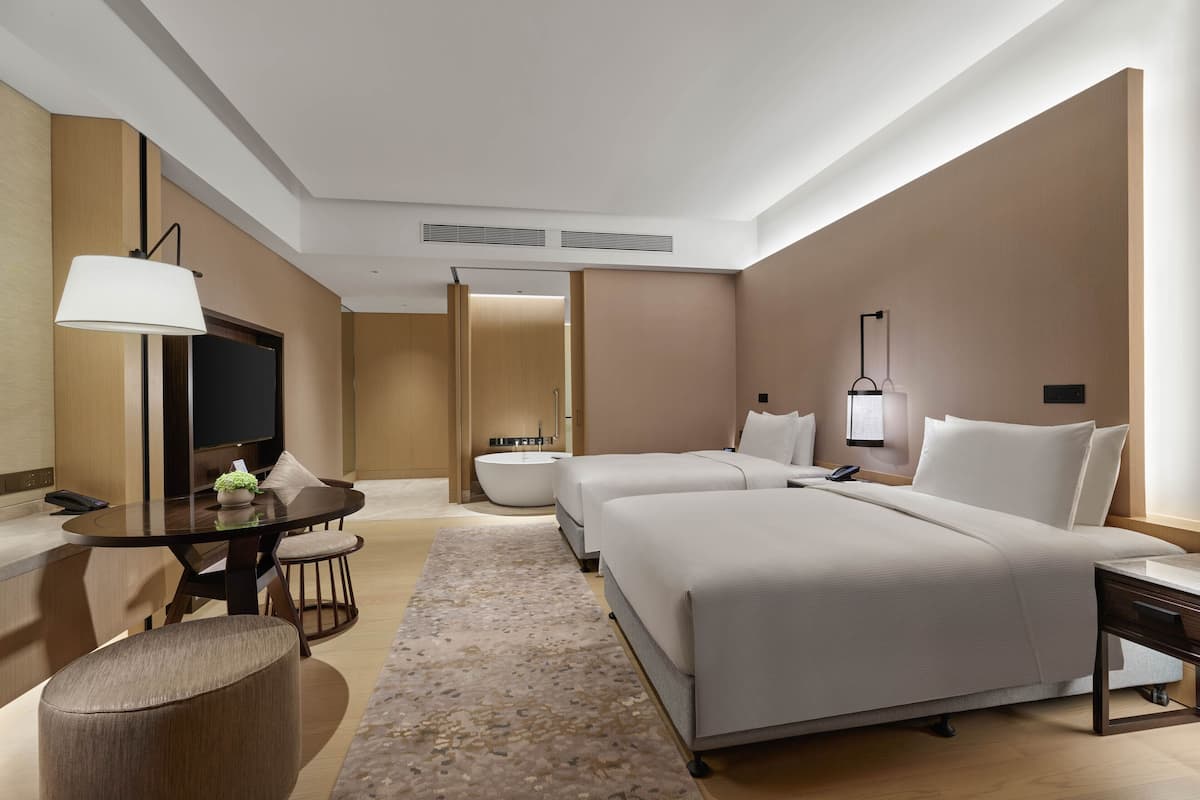 A modern hotel room with a large bed, a separate seating area with a table and chairs, a flat-screen TV, and a bathroom with a bathtub.