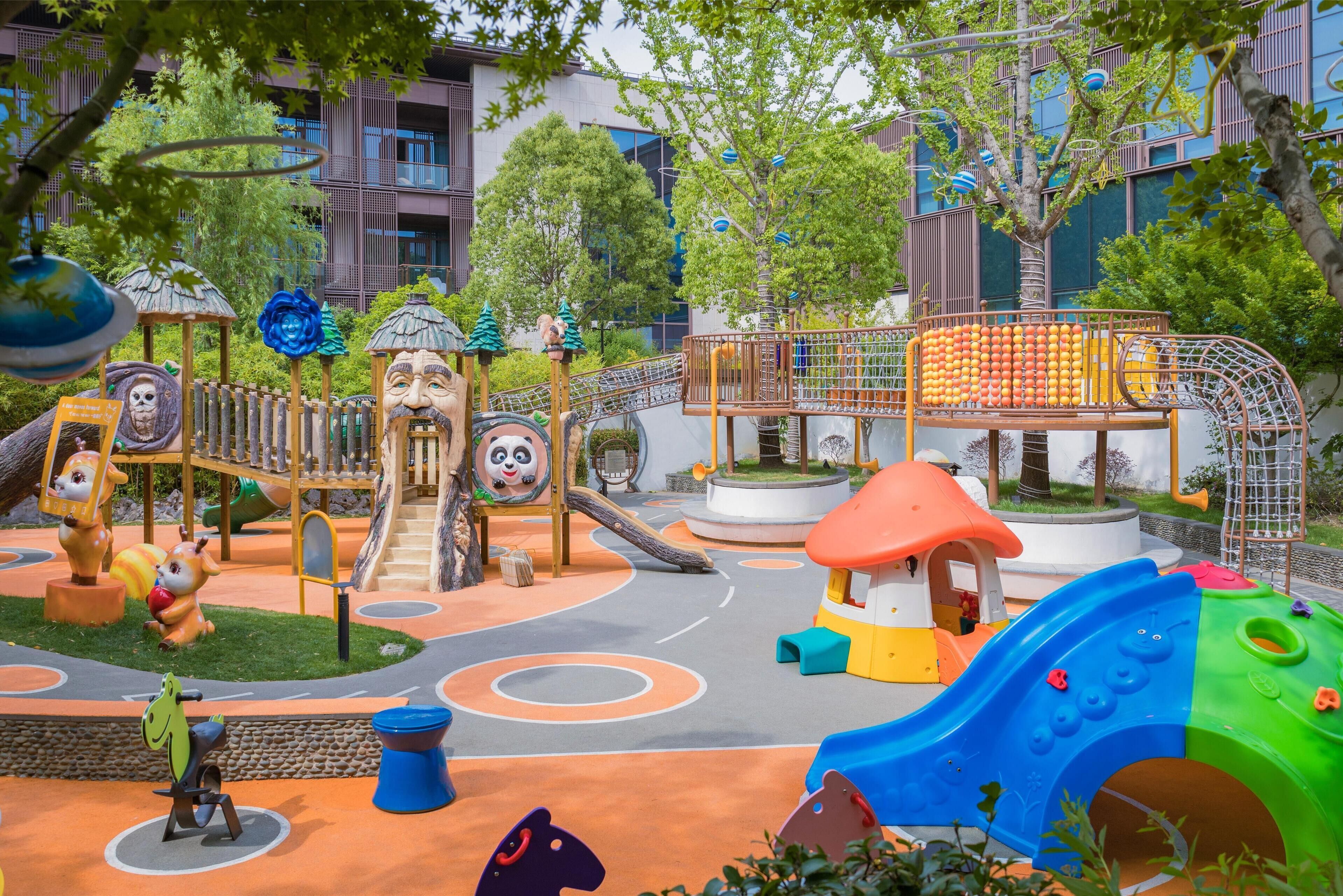 Un parque infantil con diversas estructuras de juego, incluyendo toboganes y zonas de escalada, rodeado de árboles y edificios.