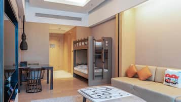 Una habitación de hotel moderna con una cama litera, un área de comedor con una mesa y sillas, un sofá con cojines y una pequeña mesa con un mantel individual.