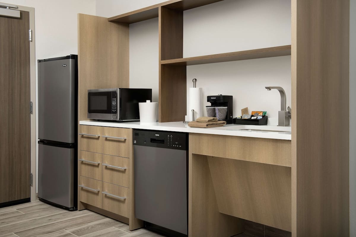 Eine moderne Küche mit einem Edelstahl-Kühlschrank, einer Mikrowelle, einem Geschirrspüler und einer Kaffeemaschine.