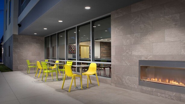 An outdoor patio with yellow chairs and a built-in fireplace. - Home2 Suites by Hilton Tampa Westshore Airport, FL (Tampa)