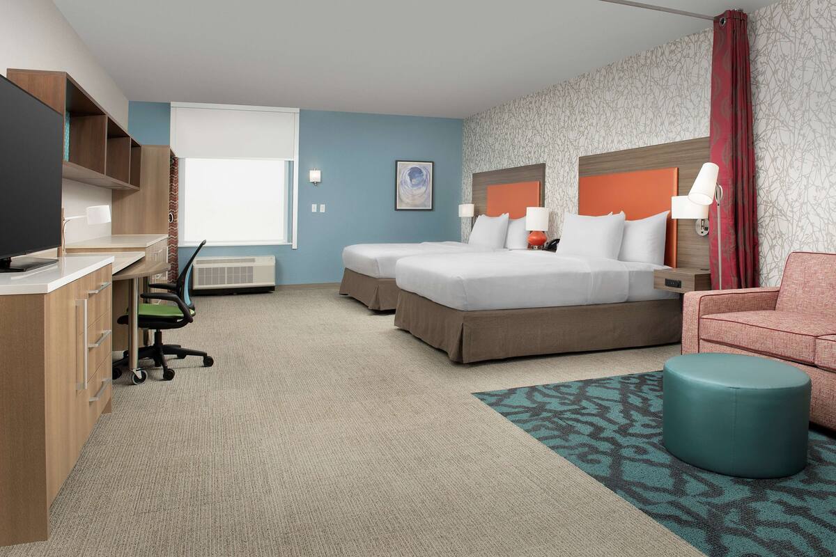 Ein Hotelzimmer mit zwei Betten, einem Schreibtisch, einem Fernseher und einem Sofa.