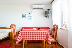 Una habitación con una mesa a cuadros, dos sillas, una cama, un televisor y cuadros en la pared.