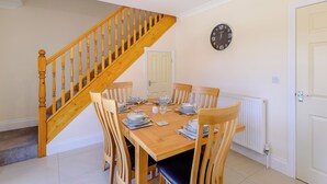 A dining area with a wooden staircase, a clock on the wall, and a white door. - Dawson Park 6 - UK12665 (Mablethorpe)