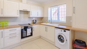 A compact kitchen with white cabinets, a built-in oven, a washing machine, and a window with blinds. - Dawson Park 6 - UK12665 (Mablethorpe)