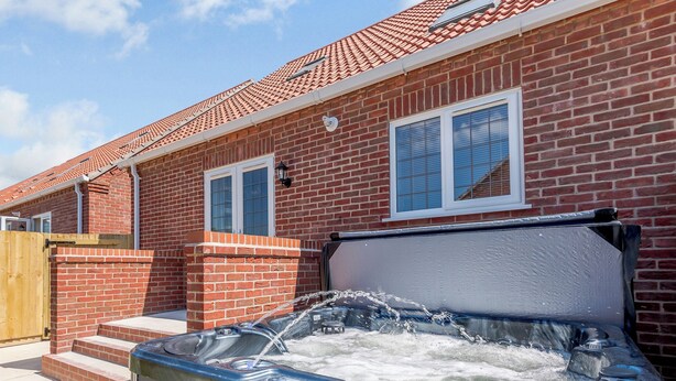 A hot tub in front of a brick house with a tiled roof and two windows. - Dawson Park 6 - UK12665 (Mablethorpe)