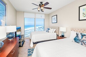 Habitación de hotel con dos camas, ventilador de techo, ventana grande con vistas y televisión.