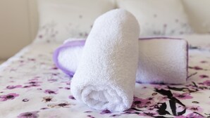 A neatly made bed with a floral-patterned bedspread and two rolled white towels placed on it.