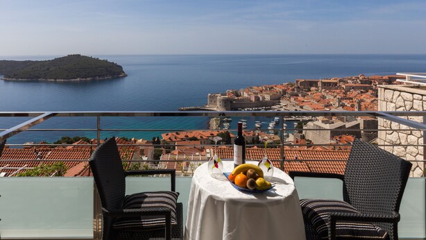 A balcony with a table set for two, overlooking a coastal town and a small island.