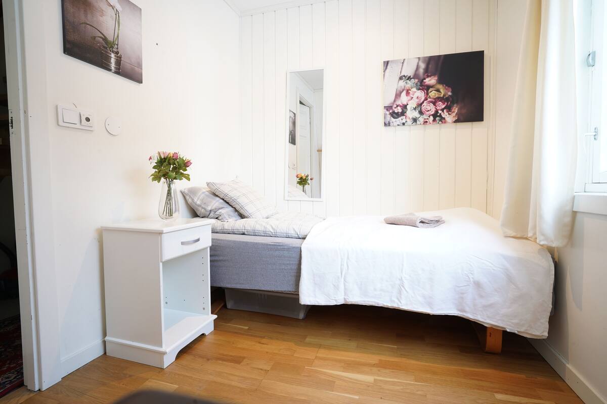 A bedroom with a bed, a bedside table, a dresser, and a mirror.