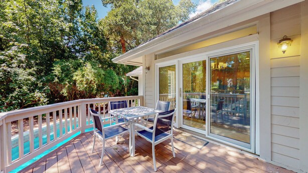 A wooden deck with a table and chairs, a glass door leading inside, and a railing.
