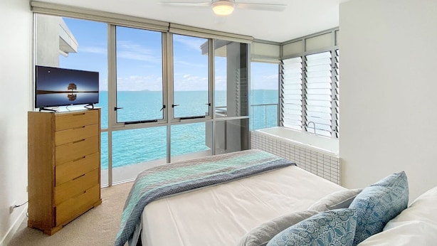 A bedroom with a bed, a dresser, a ceiling fan, and a view of the ocean. - 1 Bright Point Apartment 4502 (Nelly Bay)
