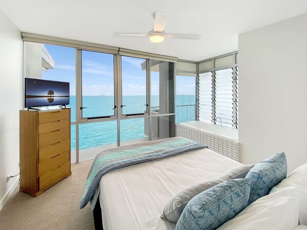 A bedroom with a bed, a dresser, a ceiling fan, and a view of the ocean. - 1 Bright Point Apartment 4502 (Nelly Bay)