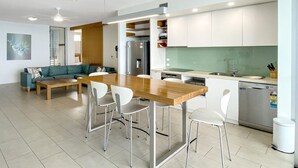 A modern kitchen with a wooden island, white chairs, and a built-in dishwasher. - 1 Bright Point Apartment 4502 (Nelly Bay)