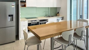 A modern kitchen with a wooden table and chairs, stainless steel appliances, and a green backsplash. - 1 Bright Point Apartment 4502 (Nelly Bay)
