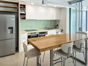 A modern kitchen with a wooden table and chairs, stainless steel appliances, and a green backsplash. - 1 Bright Point Apartment 4502 (Nelly Bay)